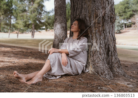 Woman Relaxing Against Tree in Peaceful Nature Setting Woman Relaxing Against Tree in Peaceful Nature Setting 136803513