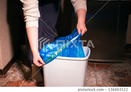 Woman placing new blue garbage bag into empty trash bin in home kitchen 136803522