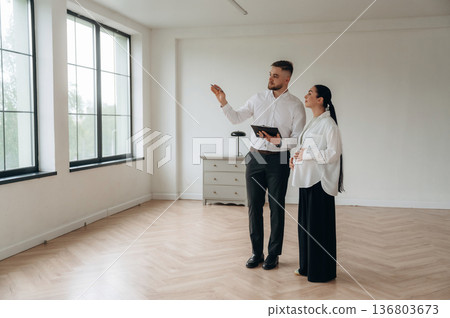 Notepad in hand, showing interior. Man and woman are in the modern new room, conception of business 136803673