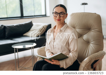 Relaxing on the chair, sitting. Woman in formal clothes is in the modern big room 136803723