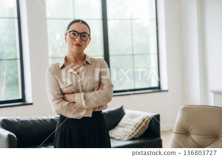 Arms crossed, standing. Woman in formal clothes is in the modern big room 136803727