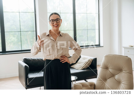 Thumb up hand gesture. Woman in formal clothes is in the modern big room 136803728