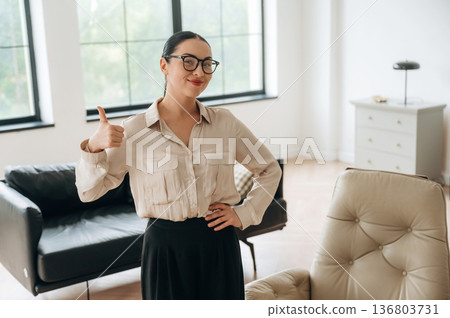Thumb up hand gesture. Woman in formal clothes is in the modern big room 136803731