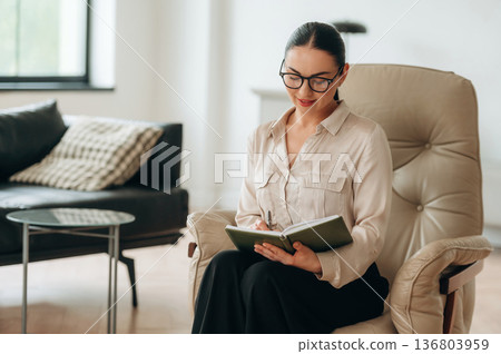Relaxing on the chair, sitting. Woman in formal clothes is in the modern big room 136803959