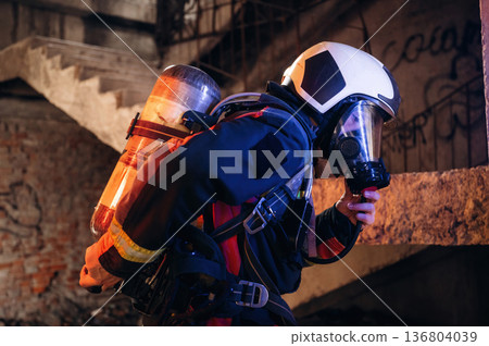 View from the side, with air balloons and mask. Firefighter in professional equipment is indoors in abandoned building 136804039