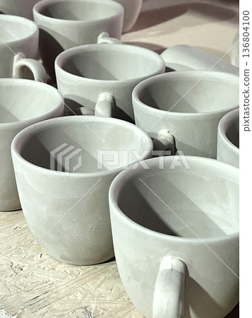 Ceramic cups are arranged neatly, freshly crafted from raw clay, ready for further finishing in a pottery studio setting 136804100