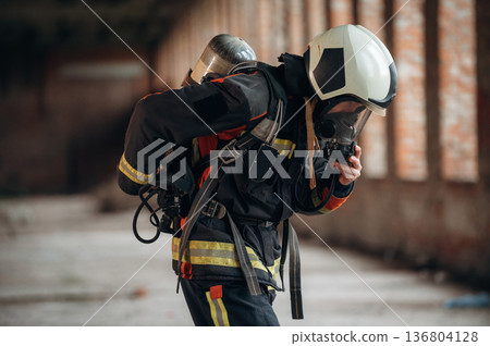 In mask, preparing air balloon. Firefighter in professional equipment is indoors in abandoned building In mask, preparing air balloon. Firefighter in professional equipment is indoors in abandoned building 136804128