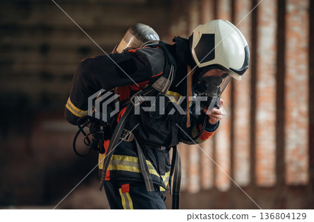 In mask, preparing air balloon. Firefighter in professional equipment is indoors in abandoned building In mask, preparing air balloon. Firefighter in professional equipment is indoors in abandoned building 136804129