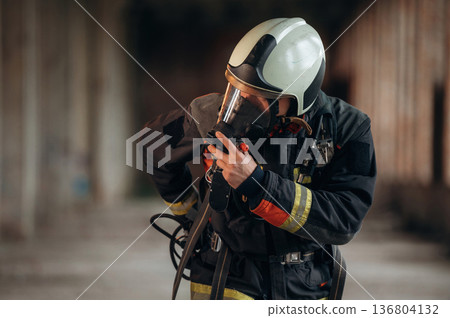 Standing in the abandoned building. Firefighter in professional equipment is indoors 136804132