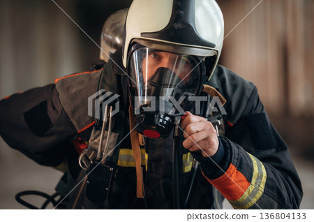 Protective air mask is on the face. Firefighter in professional equipment is indoors in abandoned building Protective air mask is on the face. Firefighter in professional equipment is indoors in abandoned building 136804133