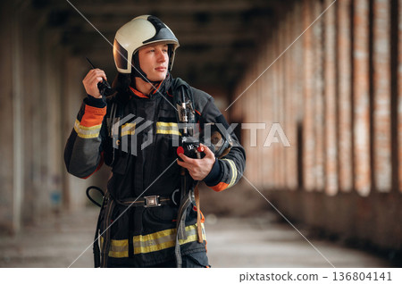 With walkie talkie radio. Firefighter in professional equipment is indoors in abandoned building With walkie talkie radio. Firefighter in professional equipment is indoors in abandoned building 136804141