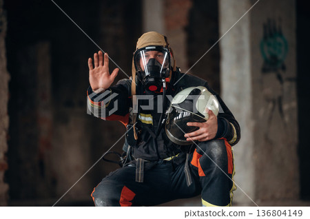 Stop hand gesture. Firefighter in professional equipment is indoors in abandoned building Stop hand gesture. Firefighter in professional equipment is indoors in abandoned building 136804149