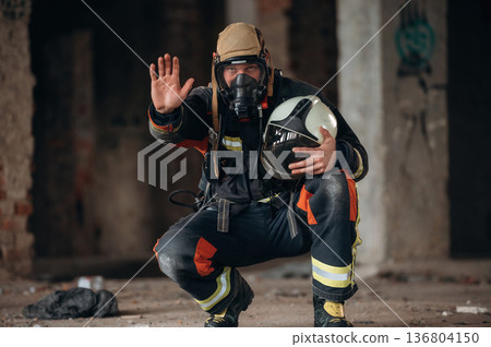 By the help of air mask. Firefighter in professional equipment is indoors in abandoned building By the help of air mask. Firefighter in professional equipment is indoors in abandoned building 136804150