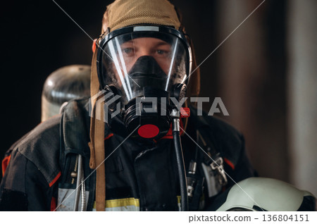 Front view, in the mask. Firefighter in professional equipment is indoors in abandoned building Front view, in the mask. Firefighter in professional equipment is indoors in abandoned building 136804151