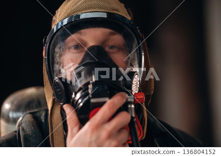 By the help of air mask. Firefighter in professional equipment is indoors in abandoned building By the help of air mask. Firefighter in professional equipment is indoors in abandoned building 136804152