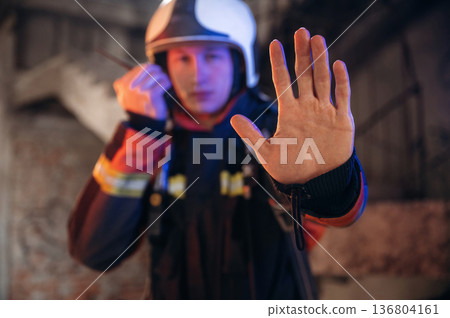 No trespassing, stop hand gesture. Firefighter in professional equipment is indoors in abandoned building No trespassing, stop hand gesture. Firefighter in professional equipment is indoors in abandoned building 136804161