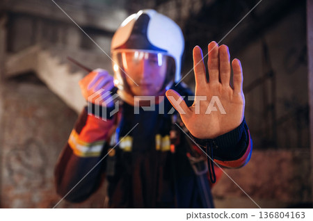 No trespassing, stop hand gesture. Firefighter in professional equipment is indoors in abandoned building 136804163