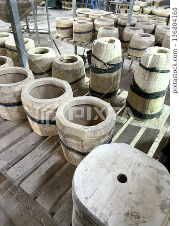 Clay vessels in various stages of completion are arranged in a ceramics workshop filled with tools and materials for shaping 136804168