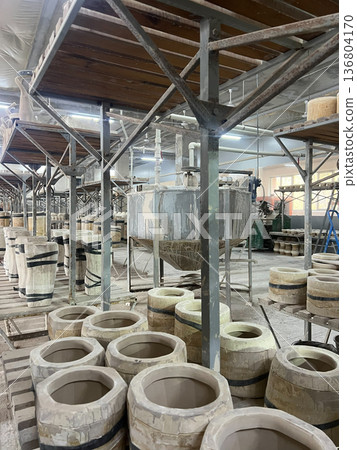 Workers are utilizing machines to shape and dry clay in a bustling ceramics workshop filled with equipment and raw materials 136804170