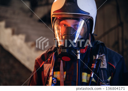 By the help of air mask. Firefighter in professional equipment is indoors in abandoned building 136804171