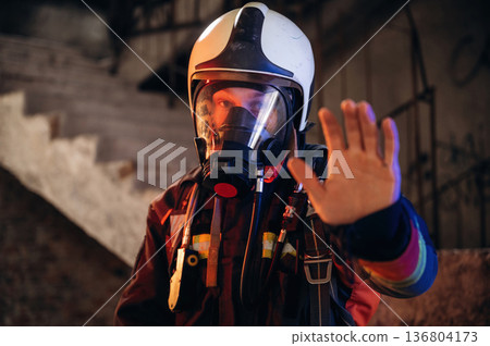 Dangerous zone, stop hand gesture. Firefighter in professional equipment is indoors in abandoned building 136804173