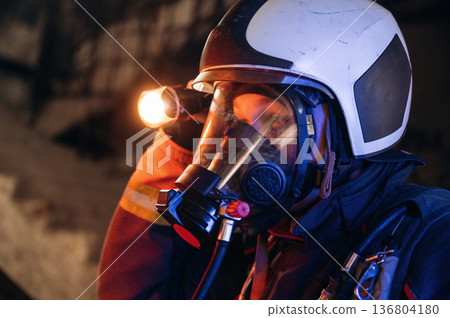 Side view, looking for the way with flashlight. Firefighter in professional equipment is indoors in abandoned building Side view, looking for the way with flashlight. Firefighter in professional equipment is indoors in abandoned building 136804180