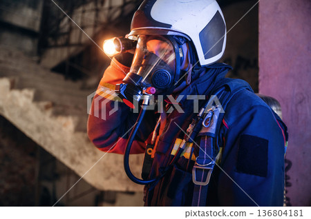 Side view, looking for the way with flashlight. Firefighter in professional equipment is indoors in abandoned building 136804181