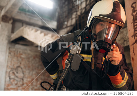 Firefighter in professional equipment is indoors in abandoned building 136804185