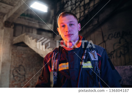 Against old stairs. Firefighter in professional equipment is indoors in abandoned building 136804187