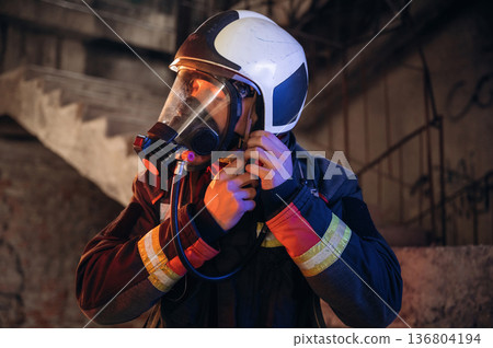 Ready, using a mask. Firefighter in professional equipment is indoors in abandoned building 136804194