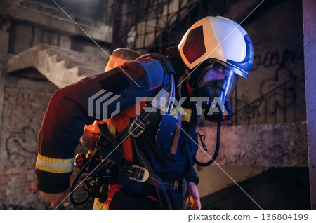 Adjusting air flow into the mask. Firefighter in professional equipment is indoors in abandoned building 136804199