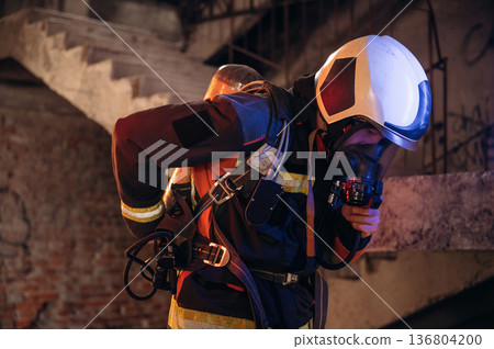 Adjusting air flow into the mask. Firefighter in professional equipment is indoors in abandoned building 136804200