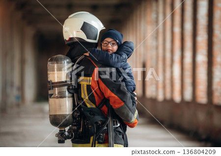 Holding kid in hands. Firefighter is with baby boy indoors Holding kid in hands. Firefighter is with baby boy indoors 136804209