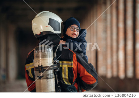 Holding kid in hands. Firefighter is with baby boy indoors Holding kid in hands. Firefighter is with baby boy indoors 136804210