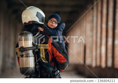 Modern hero is holding kid. Firefighter is with baby boy indoors 136804211