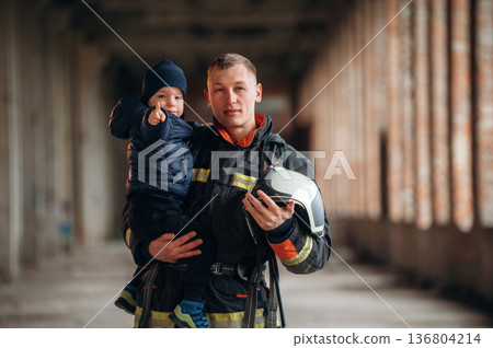 Modern hero is holding kid. Firefighter is with baby boy indoors 136804214