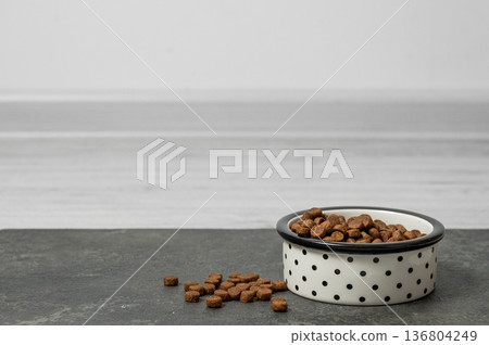 A bowl of dry dog or cat food on a gray wooden floor. 136804249