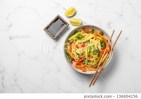 Vegetarian wok noodles with vegetables and lime in a plate on a light marble background 136804256