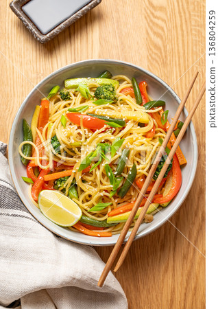 Stir fry wok noodles with vegetables in a plate on wooden countertop with chopsticks Stir fry wok noodles with vegetables in a plate on wooden countertop with chopsticks 136804259