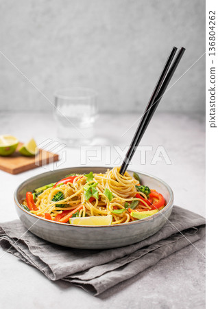 Stir fry wok noodles with vegetables in a plate on a light concrete background with chopsticks Stir fry wok noodles with vegetables in a plate on a light concrete background with chopsticks 136804262