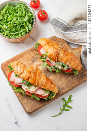 Two croissant sandwiches with ham, mozzarella cheese and arugula on a wooden board Two croissant sandwiches with ham, mozzarella cheese and arugula on a wooden board 136804271