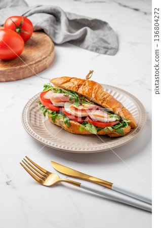 Croissant sandwich with ham, mozzarella cheese and arugula on a plate on a marble background Croissant sandwich with ham, mozzarella cheese and arugula on a plate on a marble background 136804272