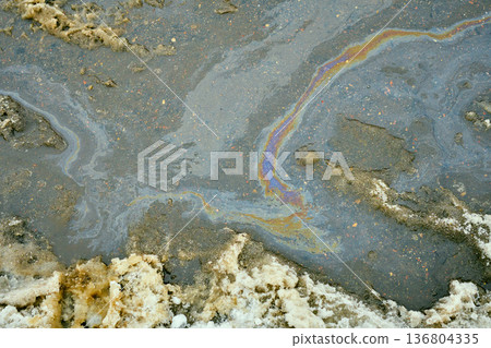 Iridescent oil slick spreading in a dirty asphalt puddle, causing environmental pollution and chemical waste 136804335