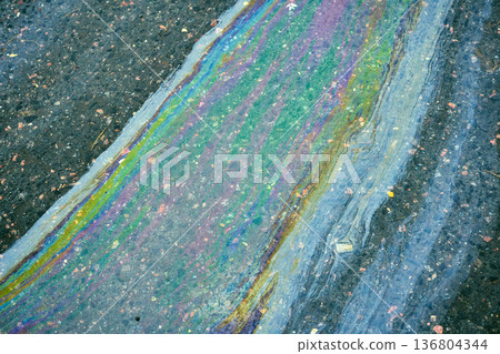 Oil spill on wet asphalt showing colorful iridescent gasoline film in sunlight. Concept of environmental pollution and danger 136804344