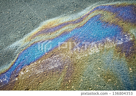 Colorful fuel puddle creating shimmering iridescent patterns on the surface of dark asphalt. 136804353