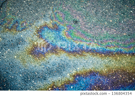 Rainbow-like oil spill creating captivating designs on the wet asphalt surface. Rainbow-like oil spill creating captivating designs on the wet asphalt surface. 136804354