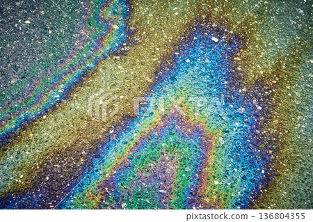 Oil spill forming an iridescent rainbow pattern on wet asphalt, showing environmental pollution 136804355
