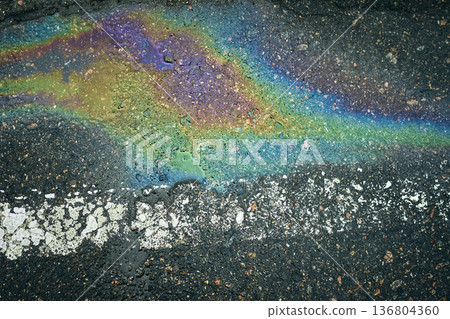 Oil spill creating a colorful rainbow pattern on wet dark asphalt with a white line. 136804360