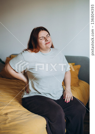 Sad Woman complaining suffering back ache sitting on uncomfortable bad at home 136804393