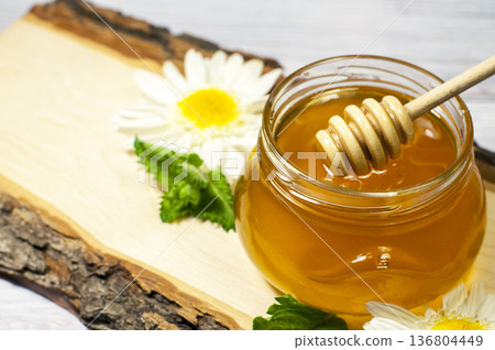 fresh honey in a jar on a wooden log with daisies 136804449